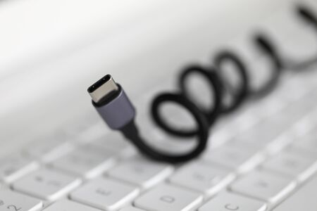 Close-up of connector lying on keyboard of laptop. Accessories for smartphone, tablet, computer. Connecting USB cable to laptop. Technology and fast charge conceptの写真素材