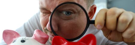 Man examining tree funny piggybanks with magnifying glass portraitの写真素材