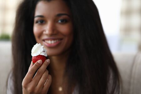 Close-up of african-american young woman holding strawberry with whipped cream. Tasty and fresh...