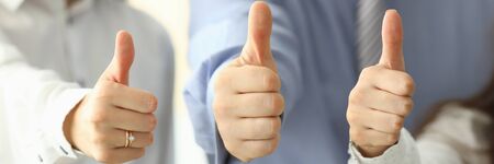 Focus on tender female and male hands showing big thumb up and posing at modern workplace. Businesspeople working in office together. Teamwork conceptの写真素材