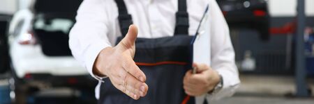 Focus on smart man hand reaching for firm handshake with someone and holding important paper folder with information about different autos. Machinery repairman conceptの写真素材