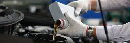 Focus on automechanic male hands in white gloves using canister of machinery liquid and precisely pouring under hood of sportcar. Automotive checkup conceptの写真素材