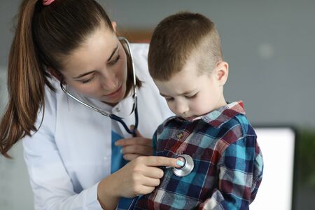 Portrait of cute woman standing and performing examination of little patient illness. Joyful child looking with interesting at stethoscope. Medicine and healthcare conceptの写真素材