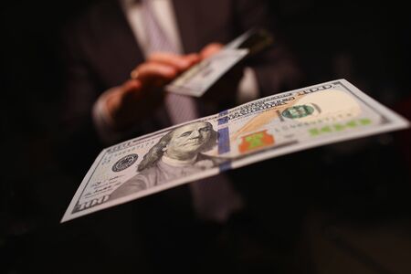 Man in business suit litter money, dollars closeup. Person spends thoughtlessly money on gambling and pleasures. Man in suit indulges his own selfish desires and buys them for money.の写真素材