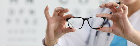 Focus on female oculist standing in clinic office and holding new glasses. Smiling ophthalmologist...
