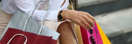 Close-up of wonderful female legs. Pretty businesswoman sitting on streets. Tender hand of woman holding stylish sunglasses. Fashion and shopping conceptの写真素材
