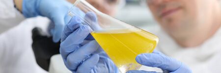 Close-up of biochemists showing on camera bright yellow liquid in glass flask. Concentrated workers...
