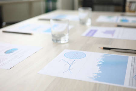 Meeting at workplace, agenda documents on table. On table in office are laid out documents with data and graphs. Meeting has been prepared in conference room to discuss data. Glasses water are table.の写真素材