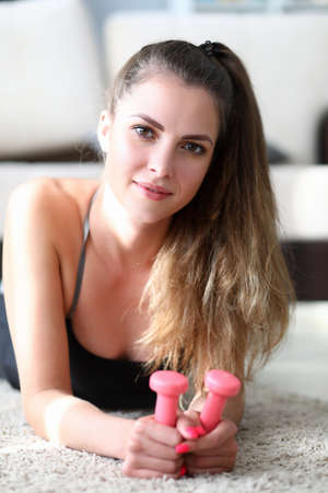 Girl in sportswear holds dumbbell in her hands. Model pays close attention to development hands....