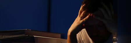 Portrait of stressed businessman sitting indoors and holding aching head with hands. Man realising...