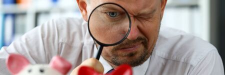 Male businessman examining group of piggybanks trying to find money portraitの写真素材