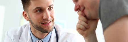 Portrait of smiling doctor reporting good news to cheerful man. Visitor looking to tablet with gladness. Medical treatment and health care concept. Blurred backgroundの写真素材