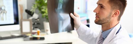 Portrait of smart doctor showing x-ray shot to worried patient. Thoughtful therapist looking at troubled male with injured leg. Medical treatment conceptの写真素材
