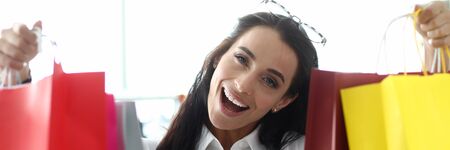 Portrait of happy woman standing in fashionable clothes boutique and looking at camera with surprise...