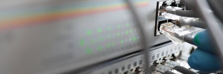 Service and networking database concept .Male technician hand in blue protective glove connects set cable connector to switch closeup.の写真素材