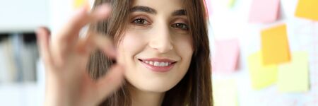Cheerful female clerk showing all right symbol with her fingers at office workplace headshot