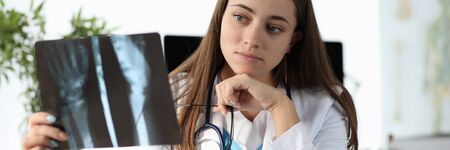 Portrait of concentrated surgeon at clinic office. Specialist with stethoscope holding radiograph of...