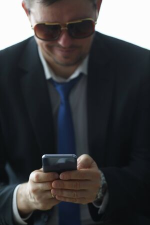 Focus on hands of man typing message on smartphone via internet app. Stylish businessman looking at...