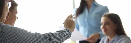 Focus on male hand holding pen. Man pointing at something with ballpen. Colleagues sitting at table in office and discussing annual report. Teamwork conceptの写真素材