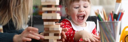 Young mum with little daughter play game in wood block against home background portrait. Happy childhood conceptの写真素材