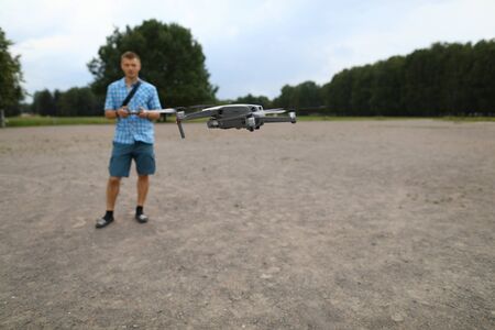 In foreground drone flies, guy controls drone. Geospatial data collection and analysis. Help field geodesy, agriculture and humanitarian aid make right decisions faster. Access to inaccessible placesの写真素材