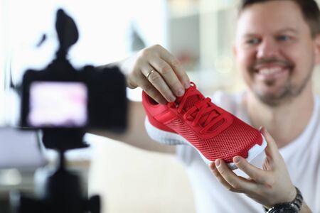 Man holds sneaker in front video camera, overview. Video blogger demonstrates appearance product and its capabilities. Creating product characteristics using animation. Quality product descriptionの写真素材