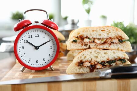 Red alarm clock with sandwich stands on wooden table closeup background. Fast food delivery concept.の写真素材