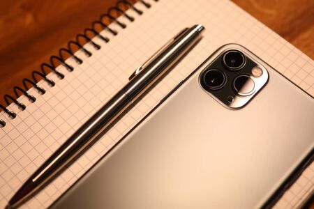 Silver smartphone and notebook with pen lie on wooden table in office close-up. Business education conceptの写真素材