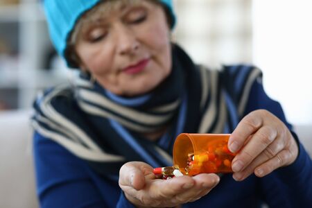 Elderly woman puts capsules from can in palm. Undesirable effects drugs. Use drug in therapeutic doses. Danger to elderly person. Serious chronic diseases frequent companion agingの写真素材