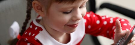 Portrait of cute girl playing with calculator at mother workspace. Smiling kid looking at electronic device with happiness and interest. Childhood and parenthood conceptの写真素材