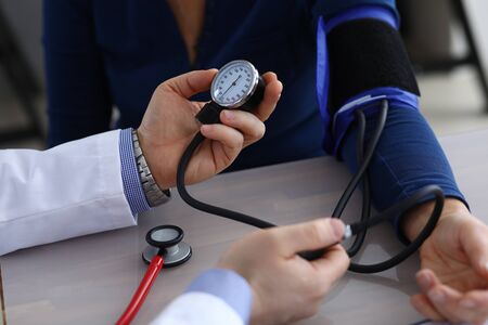Close-up of doctor hands holding tonometer and measuring pressure to ill patient. Therapist making...