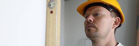 Focus on building ruler and wall. Handyman working on straightness of room. Male wearing helmet and...
