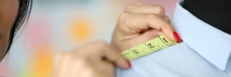 Close-up of hardworking tender hands of female tailor holding significant sewing equipment and working on project with classy blue shirt. Fashioner workshop conceptの写真素材