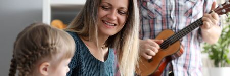 Portrait of cute parents with daughter spending time together. Happy father playing guitar, smiling...