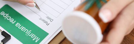 Close-up view of female doctor filling marijuana recipe for patient. Medical professional holding in hand jar with cannabis. Folk therapy and health conceptの写真素材