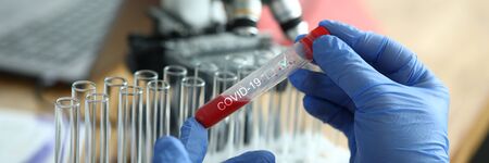 Male chemist hand in blue protective gloves hold test tube closeup background