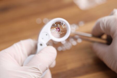 Close-up view of person looking on pink diamond through magnifying loupe. Professional in protective gloves working with precious stone. Luxury jewelry conceptの写真素材