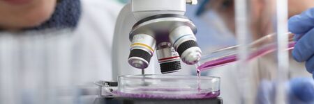 Close-up view of smiling medical colleagues making experiment with liquid. Modern microscope and...