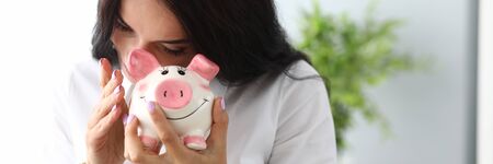 Portrait of wonderful businesslady looking into moneybox with interest and expectation. Beautiful businesswoman in fashionable blouse. Piggy bank conceptの写真素材