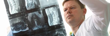 Portrait of experienced concentrated radiologist showing skiagram of back to sick woman. Doctor...