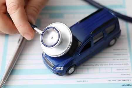Male hands holding stethoscope toy car, checking. Customs clearance. Inspection and diagnostics transport vehicles. Legal verification documents for vehicle. Car tuning registrationの写真素材