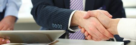 Focus on witty boss in white shirt and striped tie shaking hands with young manager. Business male perform friendly gesture towards colleague biz partner. Company meeting concept. Blurred backgroundの写真素材