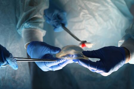 Surgeons holding instruments and breast implant. Plastic surgeon offers breast implant based on his own experience. Features choice breast implants and service life. Breast restoration for womenの写真素材