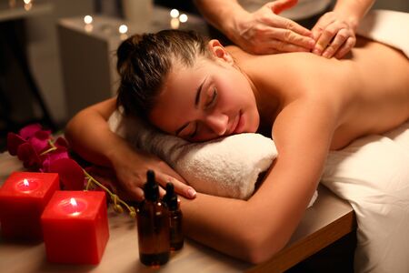 Girl relaxed lying massage, near candles and oil. Gentle caring hands master. Massage in relaxing atmosphere filled with fragrant aromas. Classic luxury massage for purpose preventionの写真素材