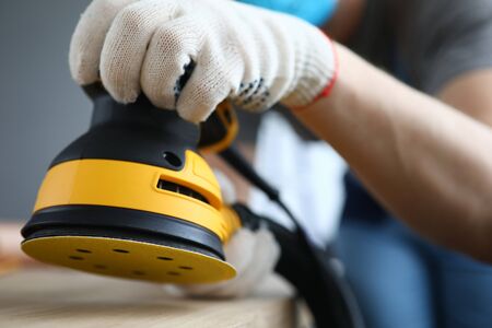 Close-up of persons hands polishing ground with grinding machine. Bright yellow sander instrument and craftsman on construction site. Protective gloves for work. Renovation conceptの写真素材