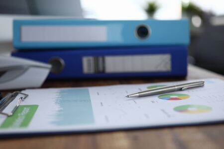 Focus on pen lying on colorful charts and graphs with significant corporation information about...