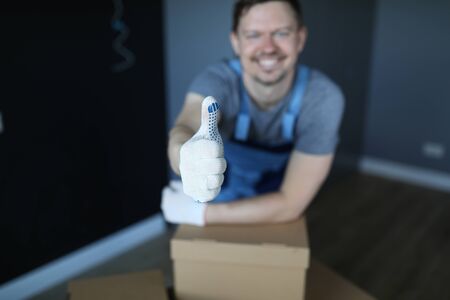 Close-up of smiling man showing thumbs-up. Cheerful male worker in empty room with carton. Well done and good job. Renovation and change interior design conceptの写真素材