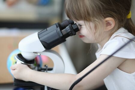 Close-up of cute child investigating sample under microscope. Kid having fun with research indoors. Spare time with exploration. Funny science and childhood conceptの写真素材