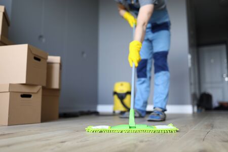 Close-up of professional cleaner washing floor with green mop. Man in working uniform. Handyman in gloves and cardboard boxes. Cleaning service and moving day conceptの写真素材