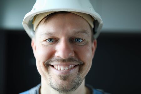 Close-up of cheerful worker face. Macro shot of foreman in protective white helmet posing on camera...